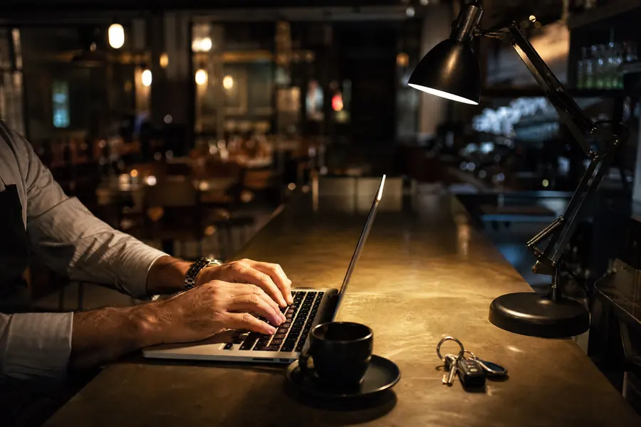 Manos del dueño escribiendo en el portátil en la barra, de noche